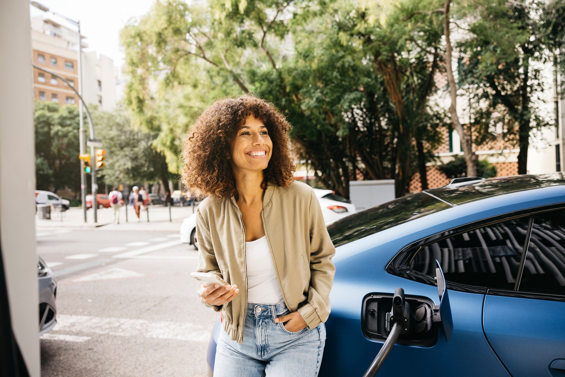 Woman smiling while charging electric car in urban setting